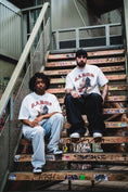 Afbeelding laden in galerij, Two people wearing the white GABOS T-shirt on stairs